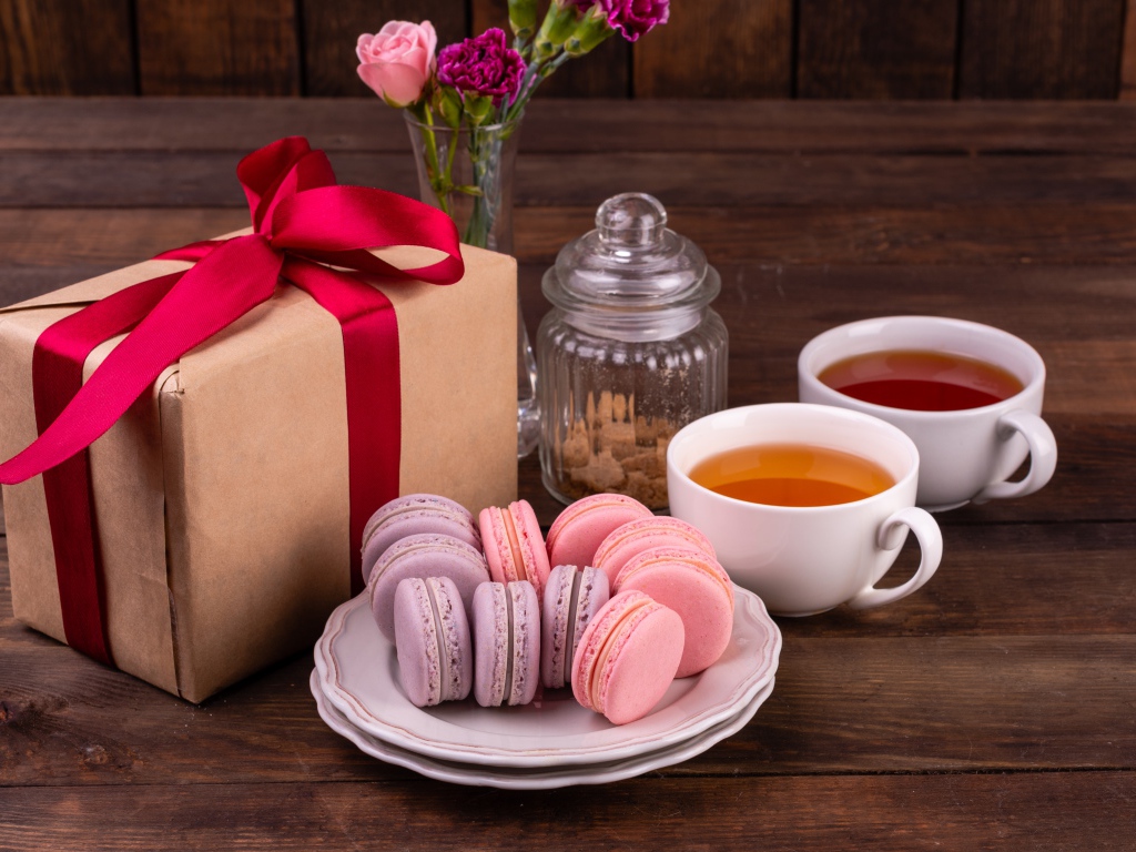 Подарок с красной лентой на столе с макарунами и чаем 