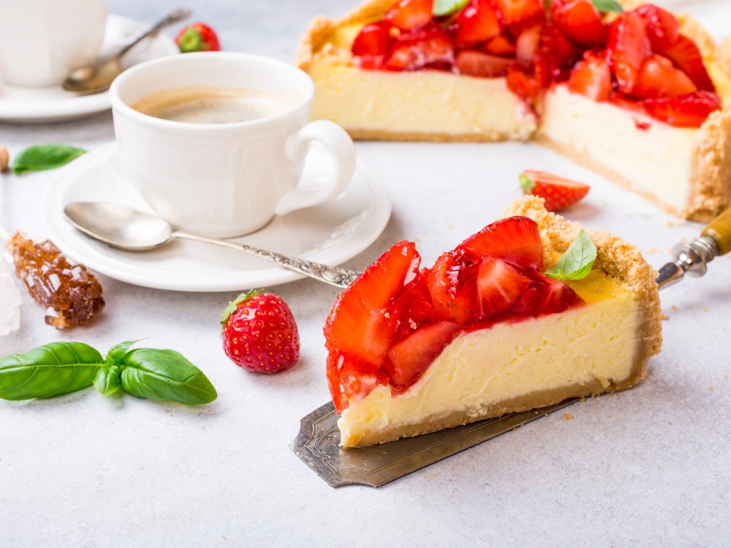 Кусок чизкейка с клубникой на столе с кофе