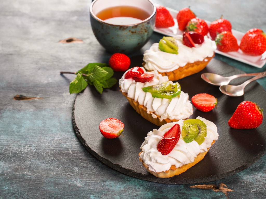 Пирожные с киви и клубникой на столе с чаем