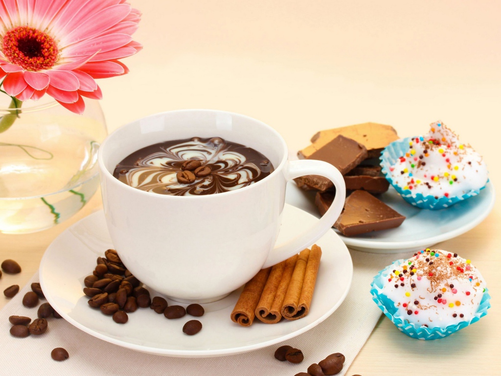 Конфеты на столе с кофе и герберой в вазе 