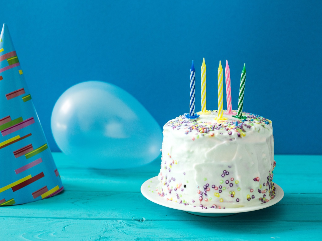 Праздничный торт со свечами, шариком и колпаком на голубом фоне
