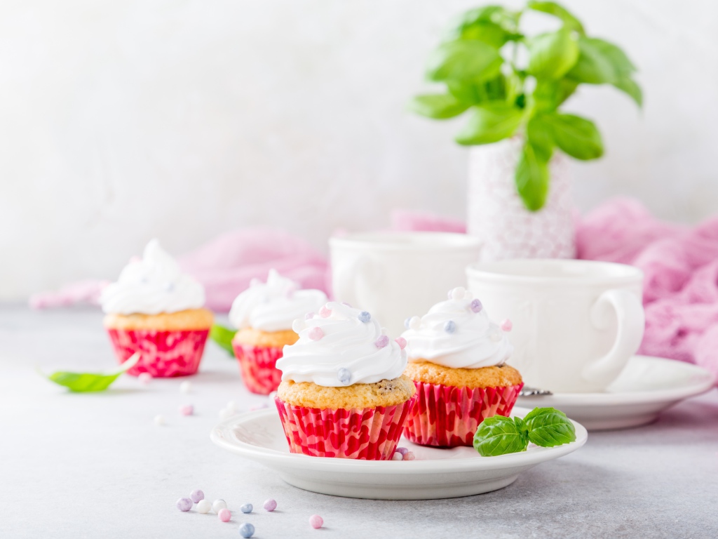 Аппетитные кексы с кремом на столе с чашками