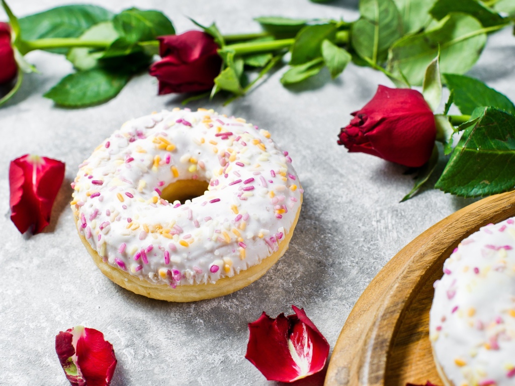 Сладкий пончик с глазурью на столе с красными розами