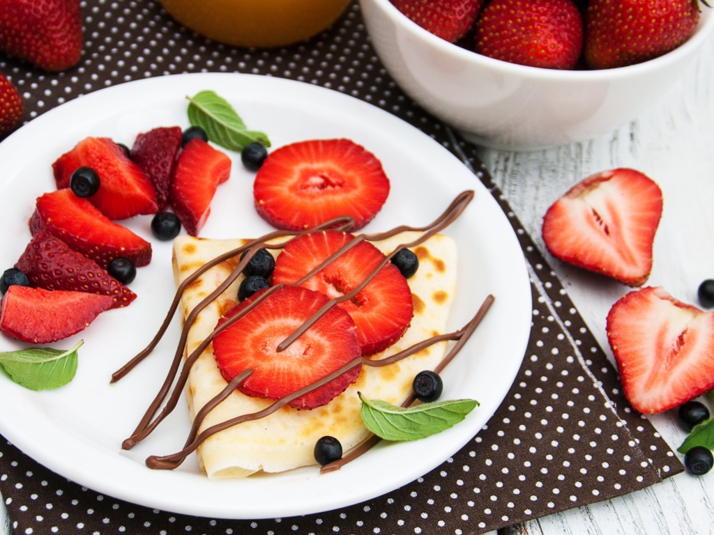 Тонкий блинчик на тарелке с шоколадом, ягодами клубники и черники