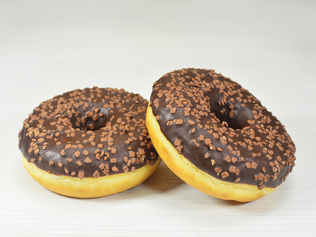 Два сладких пончика с шоколадом на сером фоне