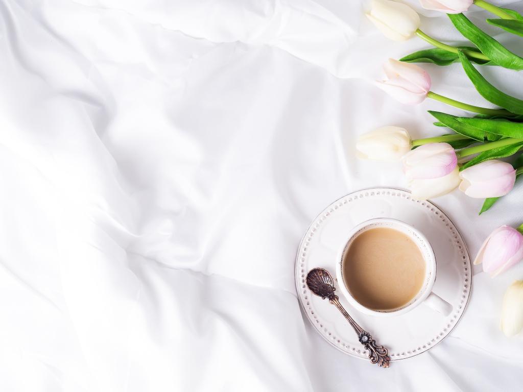 Чашка кофе на белом покрывале с тюльпанами