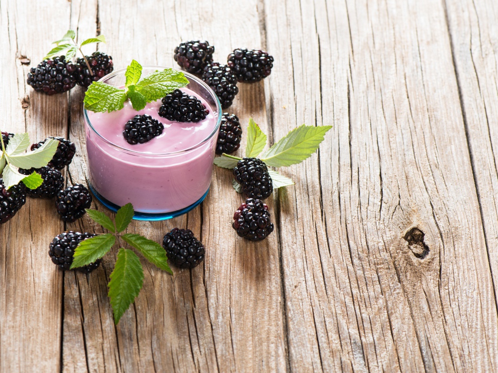 Стакан йогурта на деревянном столе с ягодами ежевики