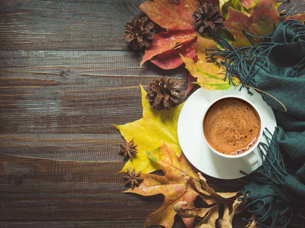 Чашка кофе на столе с шарфом, желтыми листьями и шишками