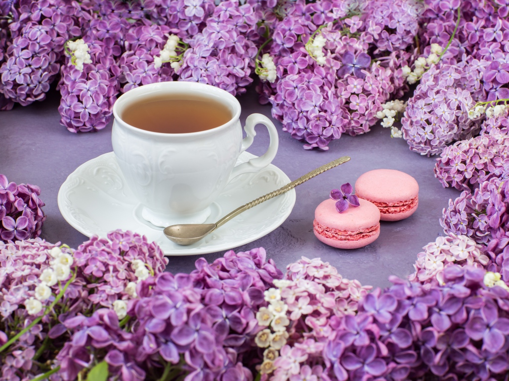 Чашка чая на столе с цветами сирени и десертом макарон