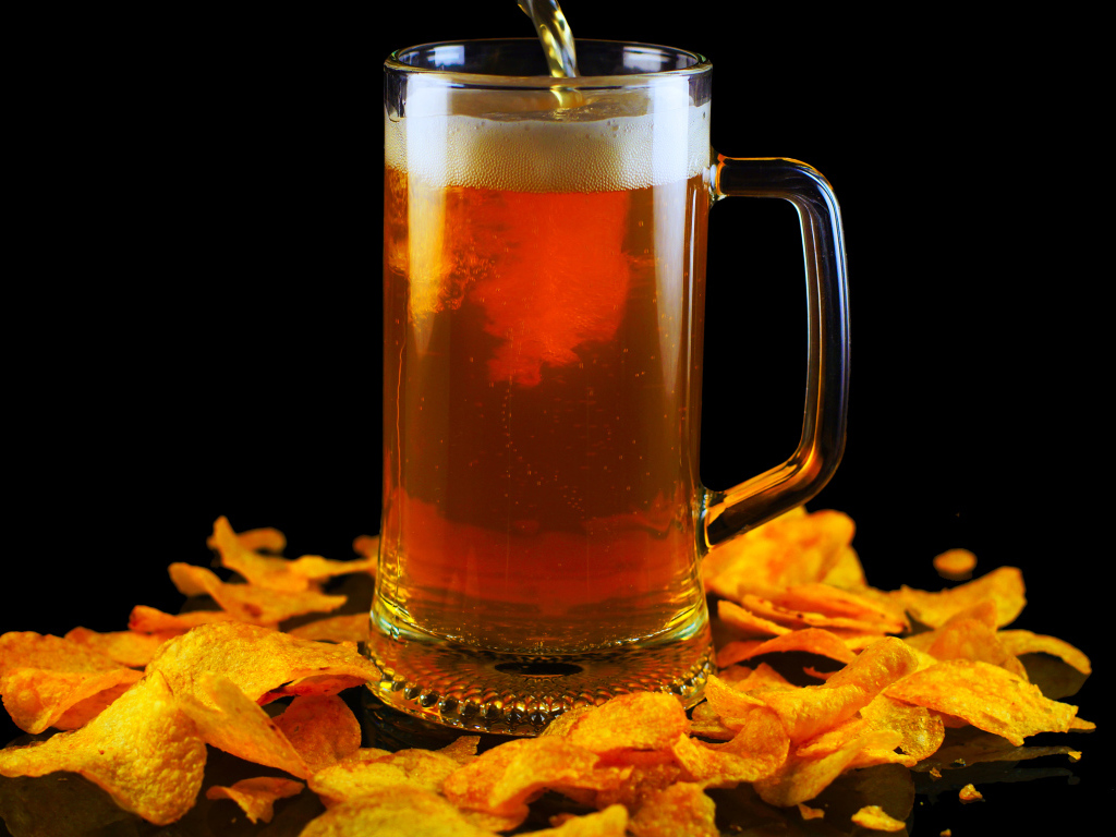 Бокал пива с чипсами на черном фоне