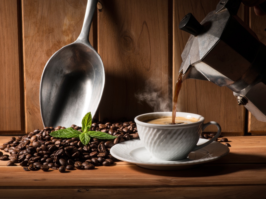 Горячий кофе наливают в белую чашку на столе с кофейными зернами