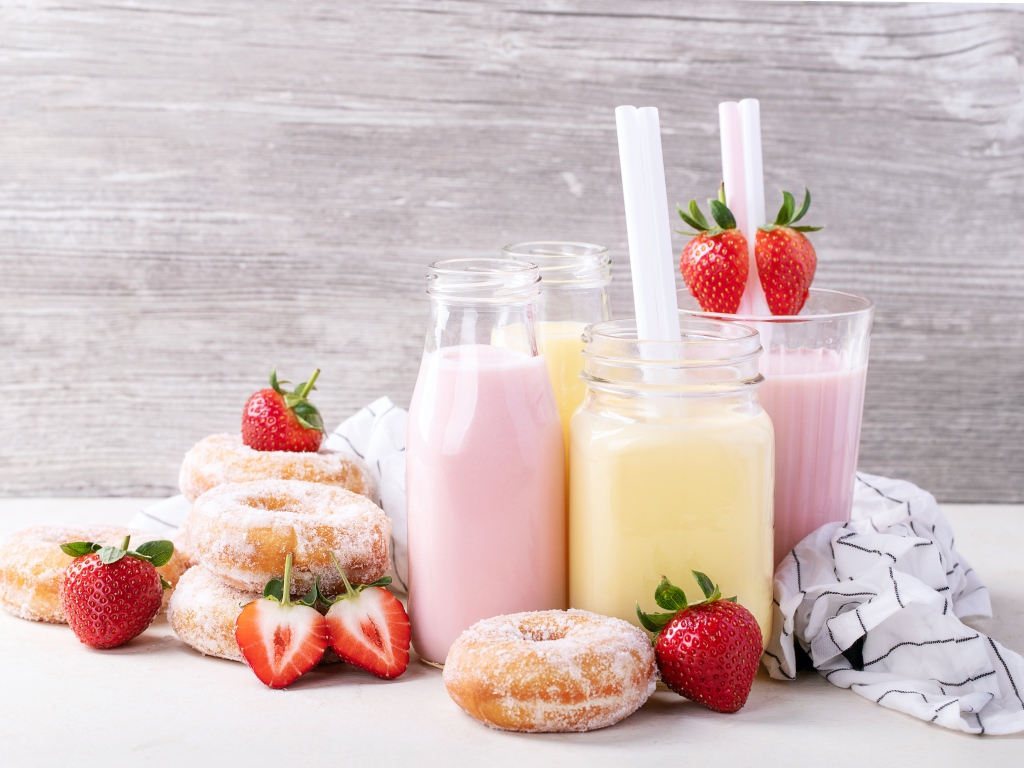 Молочные коктейли на столе с пончиками и ягодами клубники 