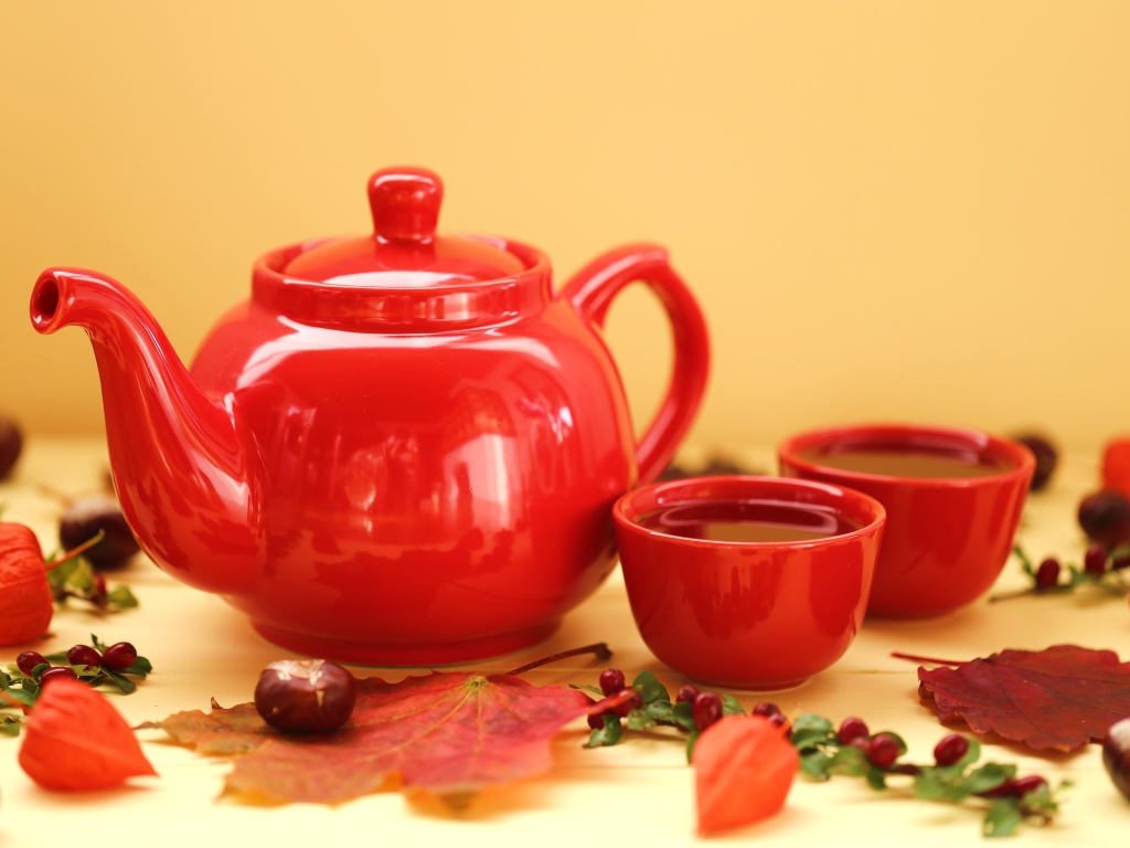 Красный чайник с чашками на столе осенью 