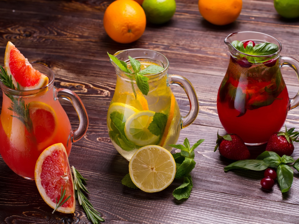 Три стеклянных графина с напитком на деревянном столе с фруктами