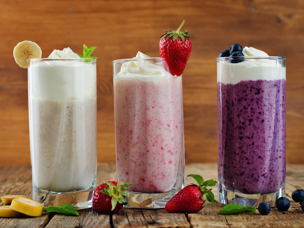 Три стакана смузи со сливками на столе с ягодами