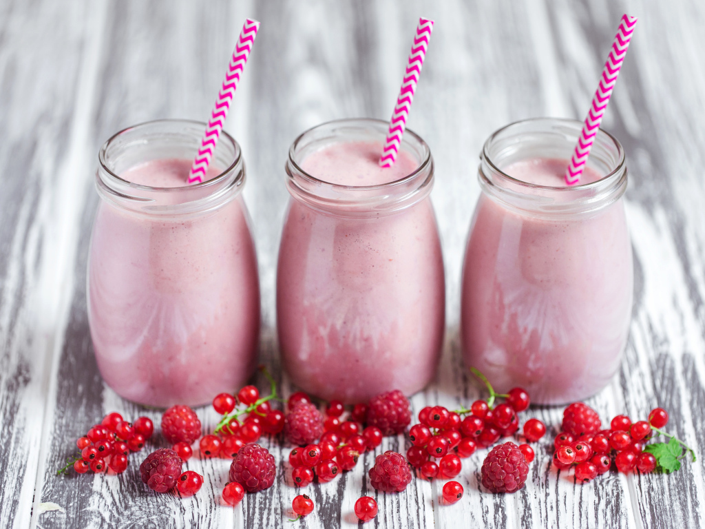 Три банки ягодного  смузи на столе с ягодами малины и смородины