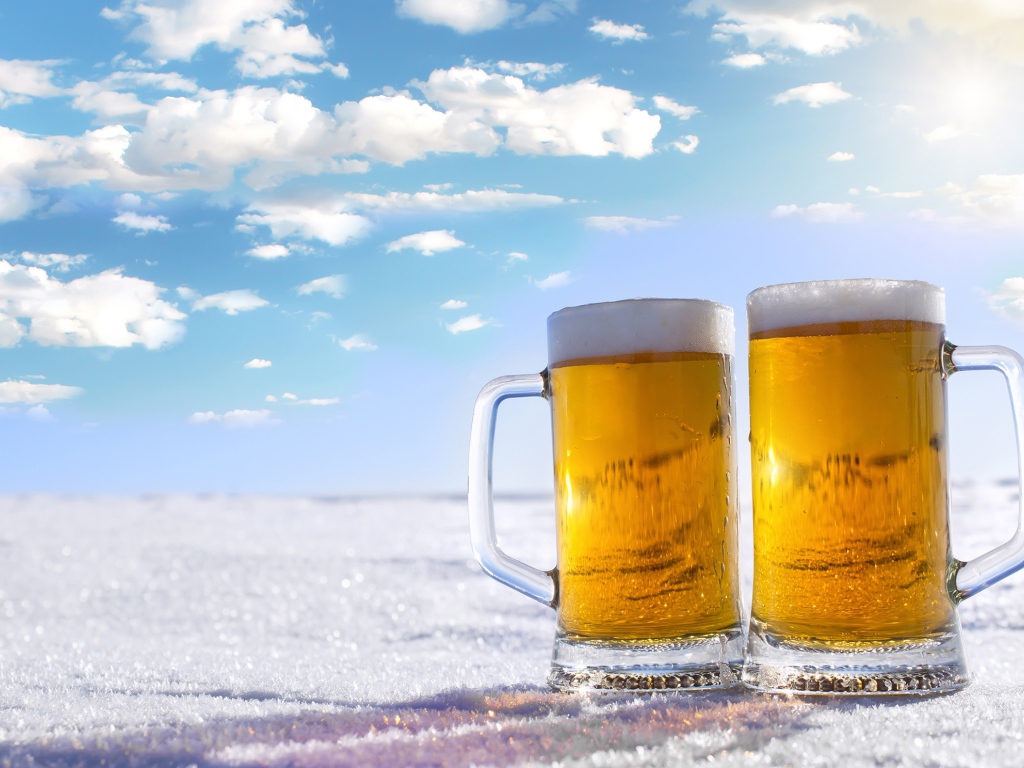 Два бокала пива стоят на белом снегу под голубым небом