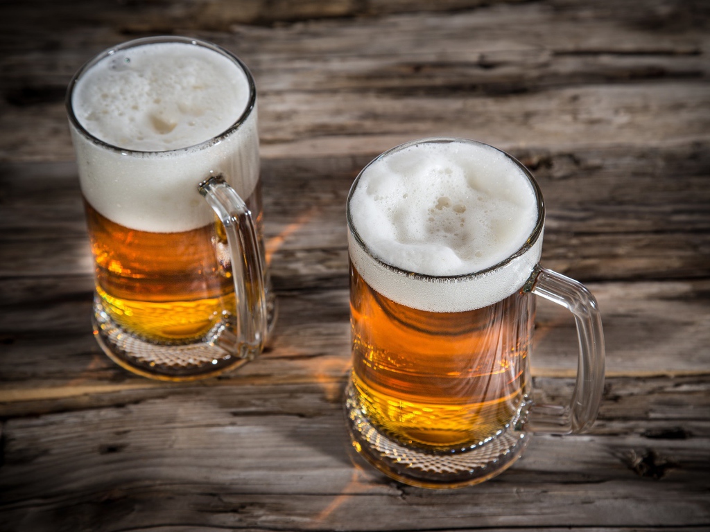 Два бокала пива с пеной на деревянном столе