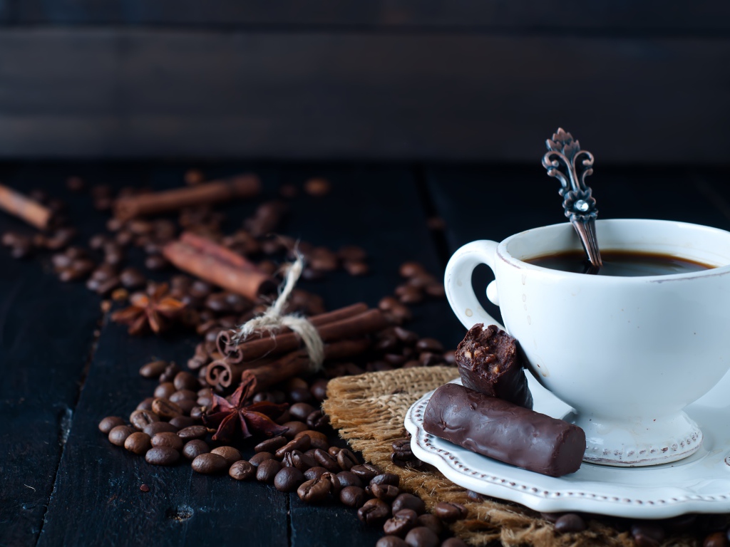 Белая чашка кофе на столе с конфетами, корицей, бадьяном и зернами