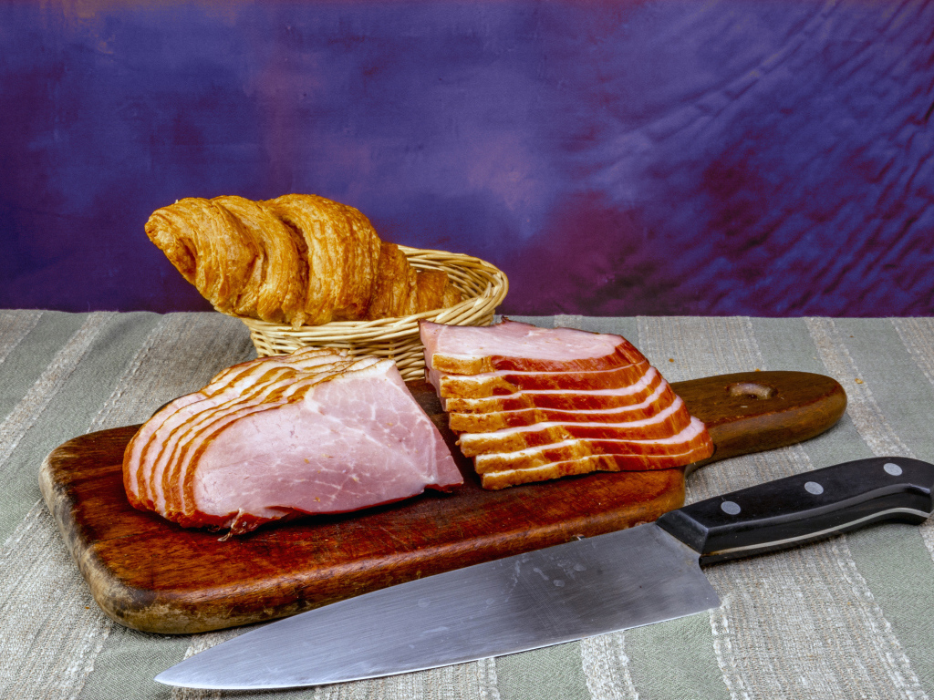 Кусок нарезанной ветчины на доске с круассаном