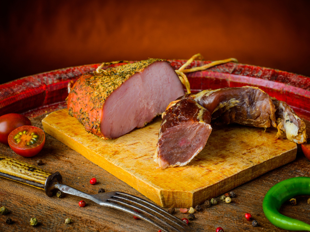 Ветчина и вяленое мясо на разделочной доске на столе с помидорами и горьким перцем 