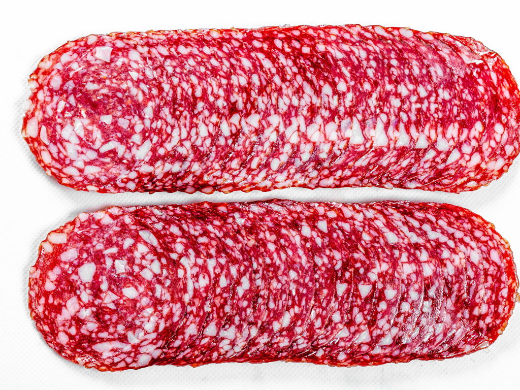 Колбаса салями нарезанная тонкими кусочками на белом фоне