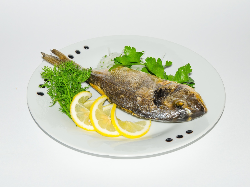 Запеченная рыба на тарелке с лимоном и зеленью 