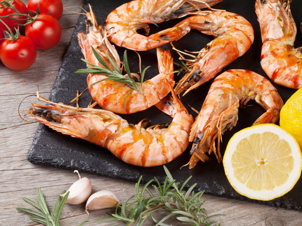 Вареные креветки на столе с лимонами и помидорами