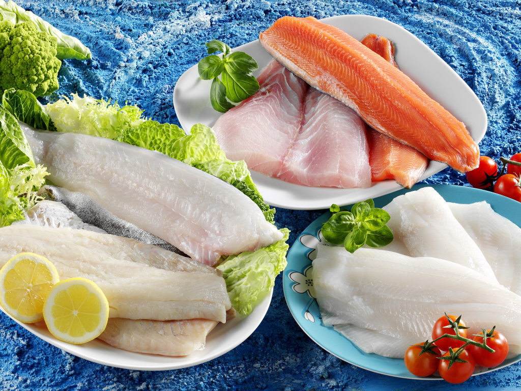 Филе рыбы на тарелках с помидорами и листьями салата