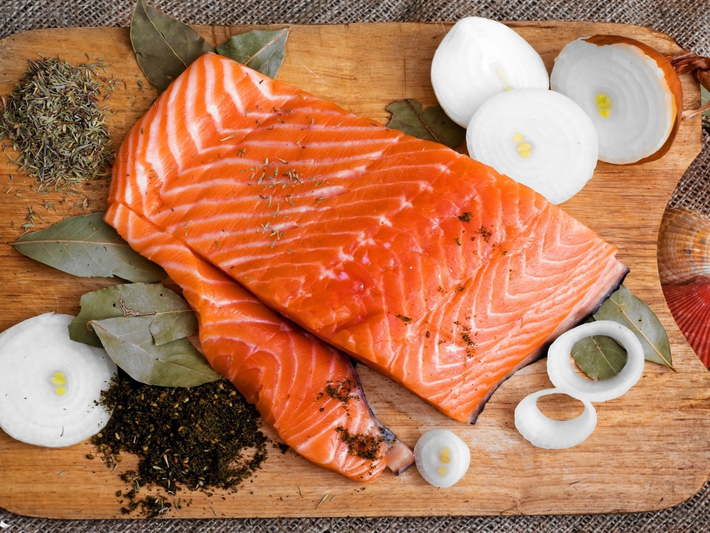 Куски красной рыбы на разделочной доске с луком и специями