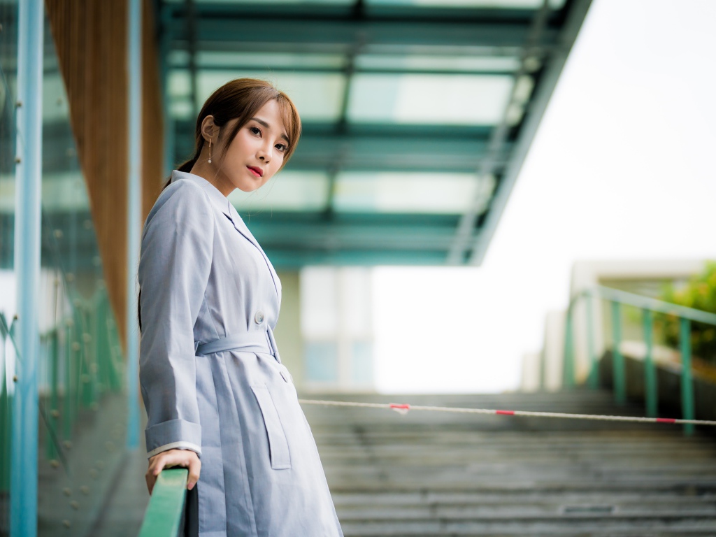 Девушка азиатка в пальто стоит у перил 