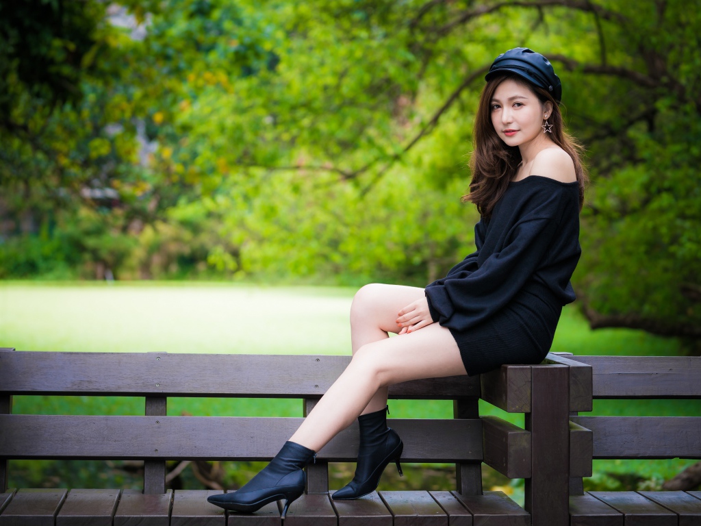 Красивая девушка азиатка в черном платье сидит на деревянной лавке