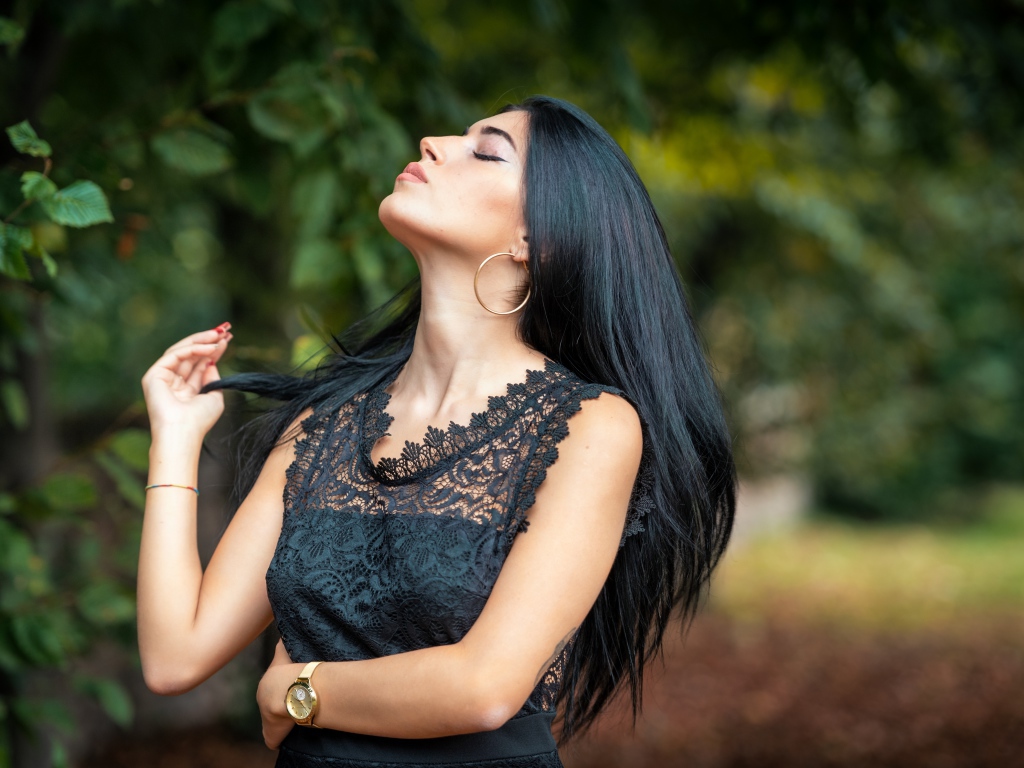 Красивая брюнетка в черном платье с закрытыми глазами в парке
