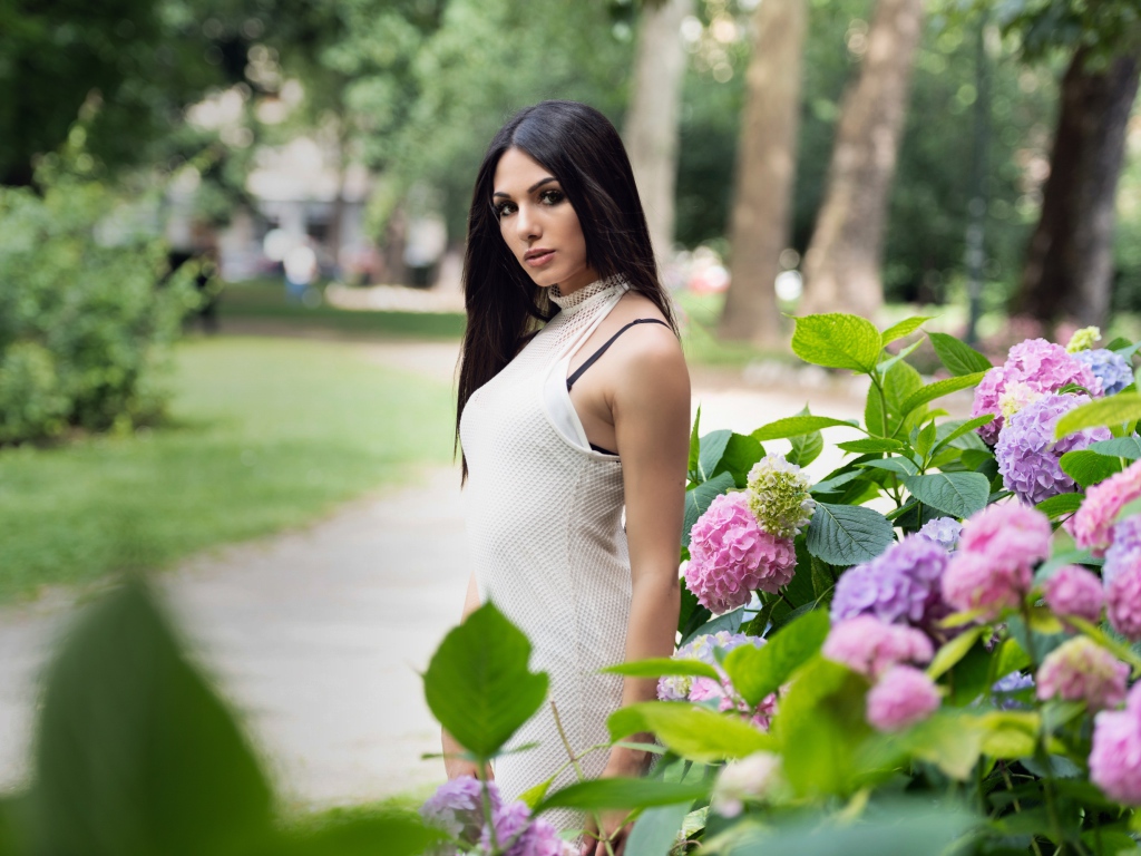 Красивая брюнетка стоит рядом с кустом гортензии