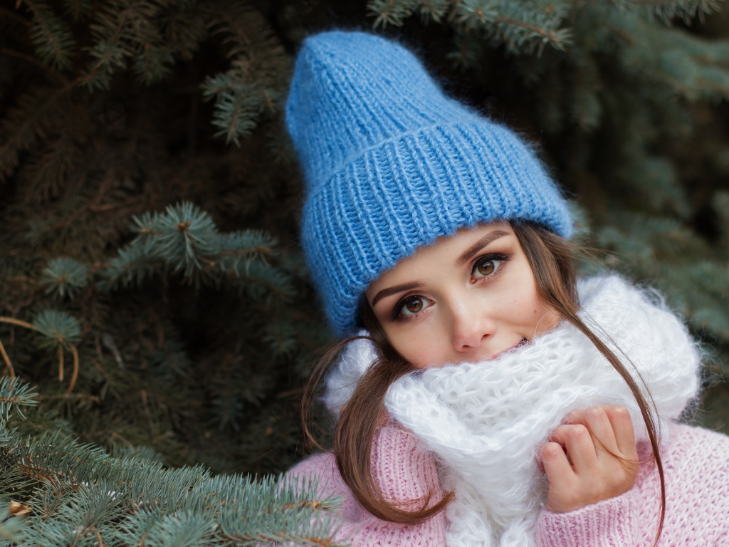 Красивая девушка с вязаной голубой шапке у ели
