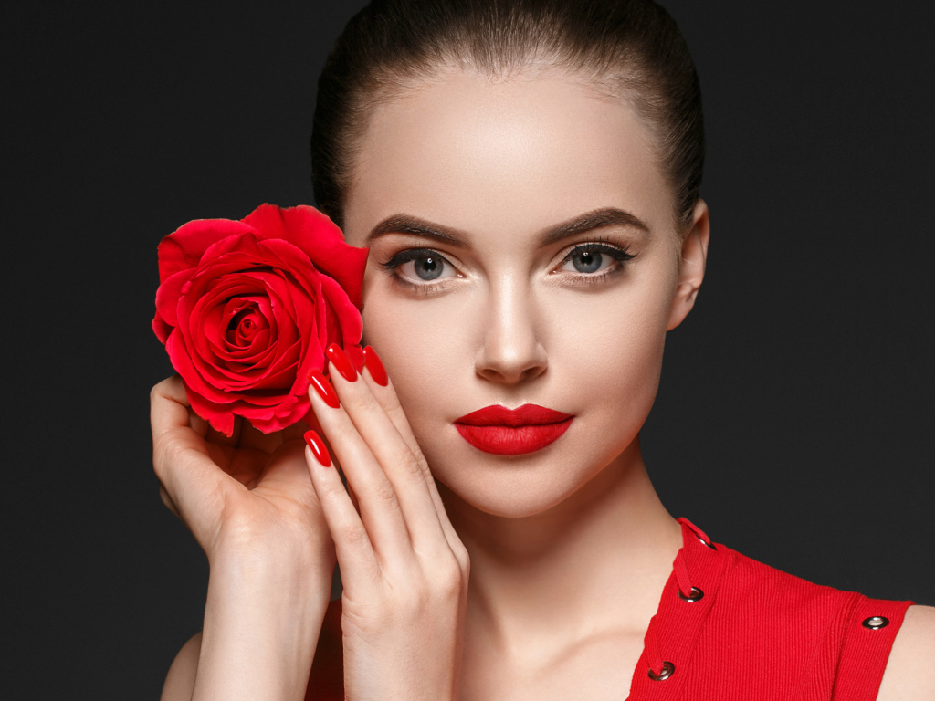 Красивая девушка с красной розой у лица на сером фоне