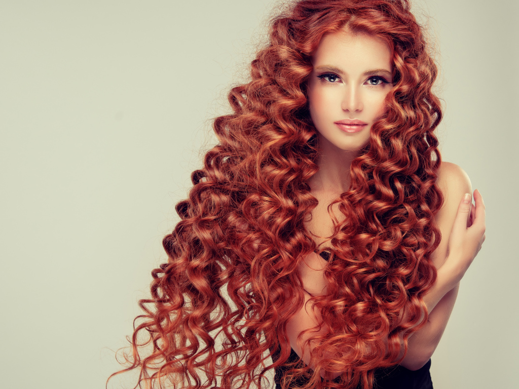 Красивая девушка с длинными рыжими волосами на сером фоне