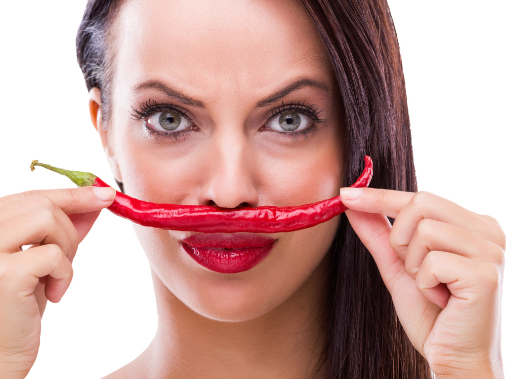Брюнетка с красным перцем у лица на белом фоне