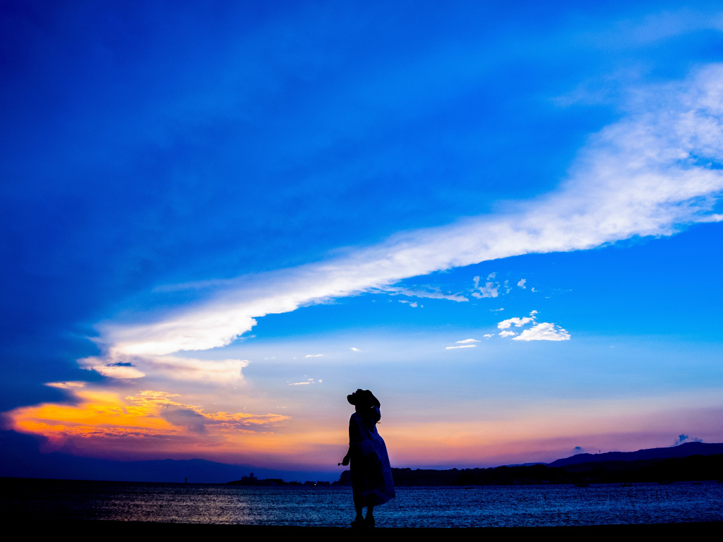 Девушка в шляпе смотрит на закат на берегу моря