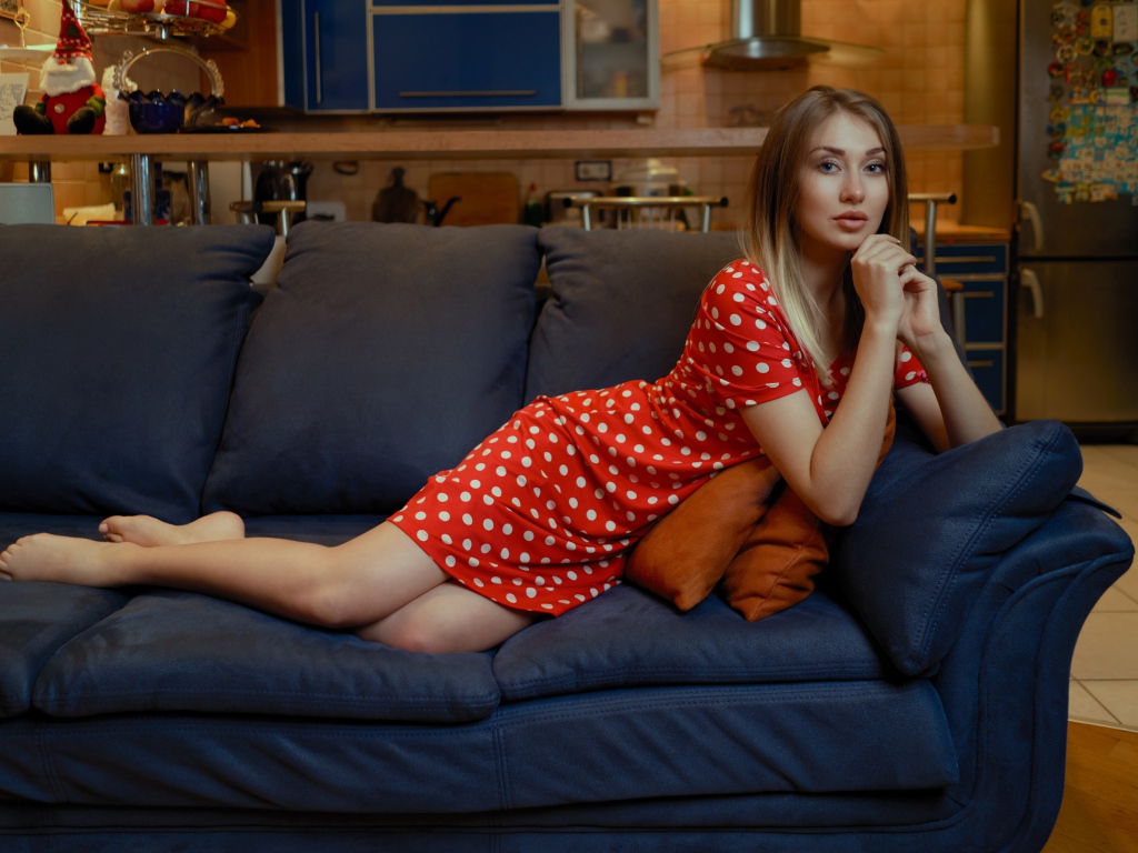 Девушка в красном платье в горошек лежит на диване