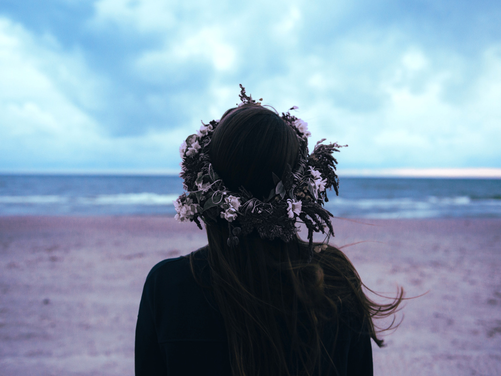 Девушка с венком на голове на фоне моря вид сзади
