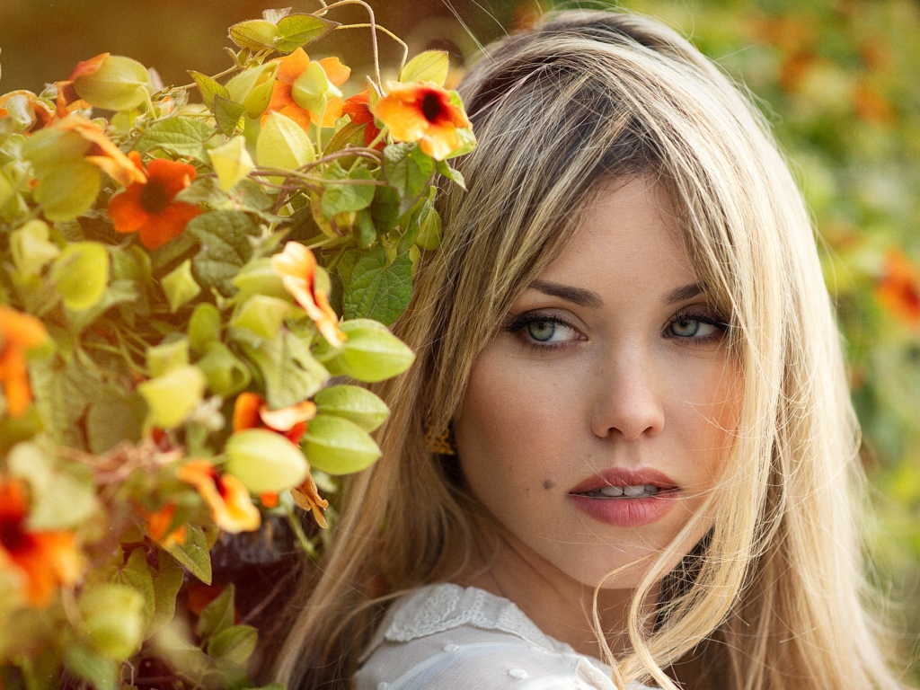 Зеленоглазая блондинка у забора с цветами 