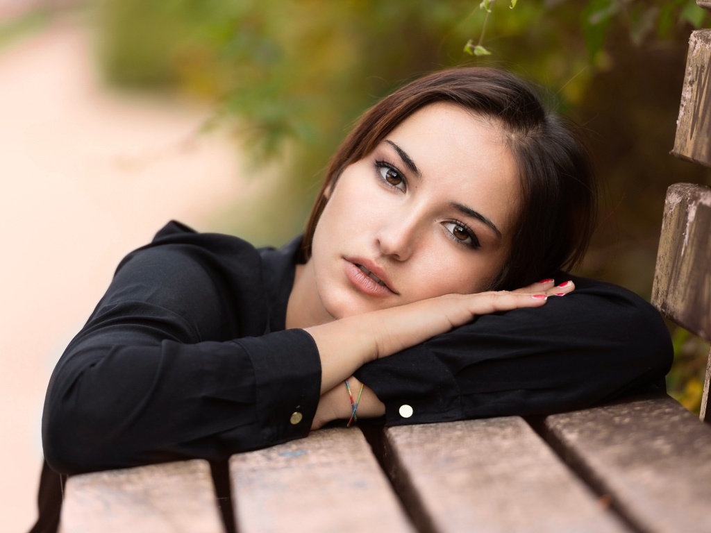 Грустная кареглазая девушка лежит на деревянной лавке