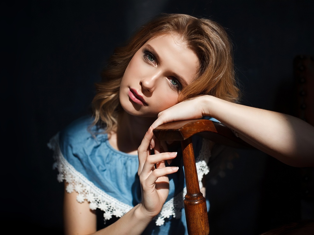 Грустная девушка сидит облокотившись об спинку кресла