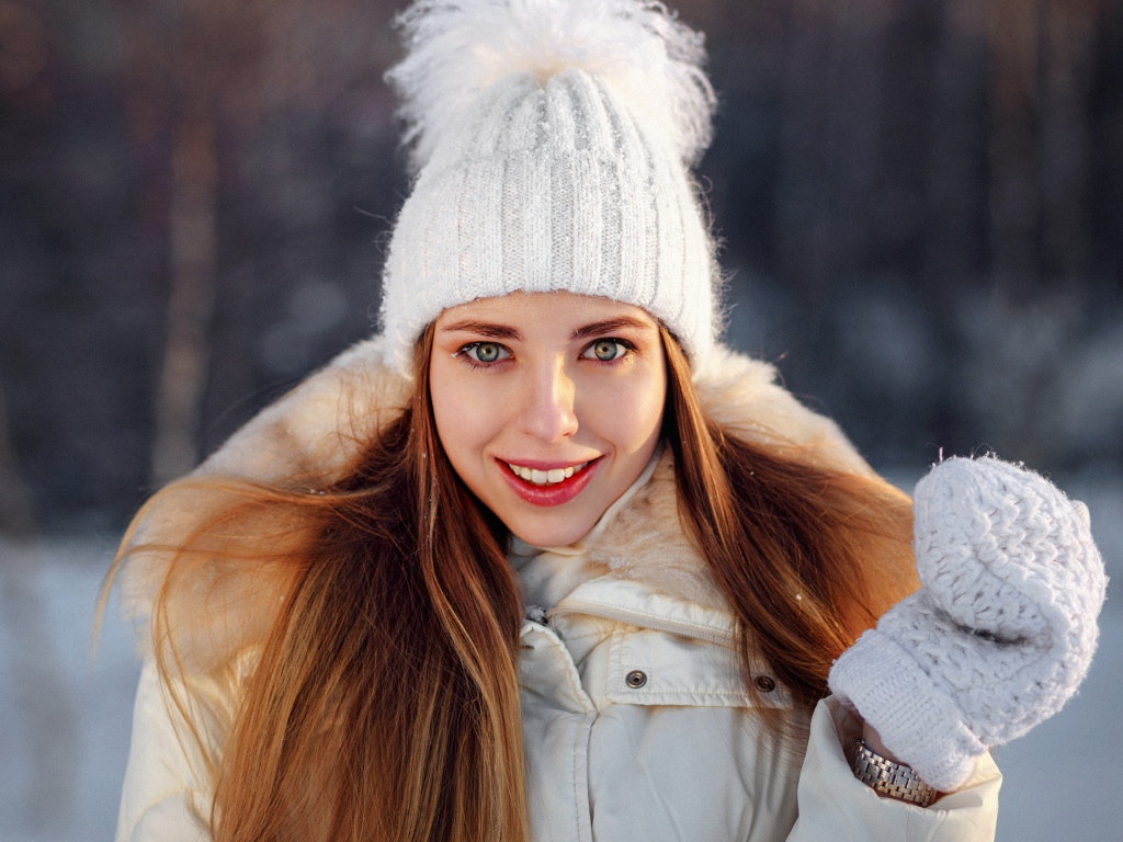 Улыбающаяся девушка в теплой шапке и варежках зимой