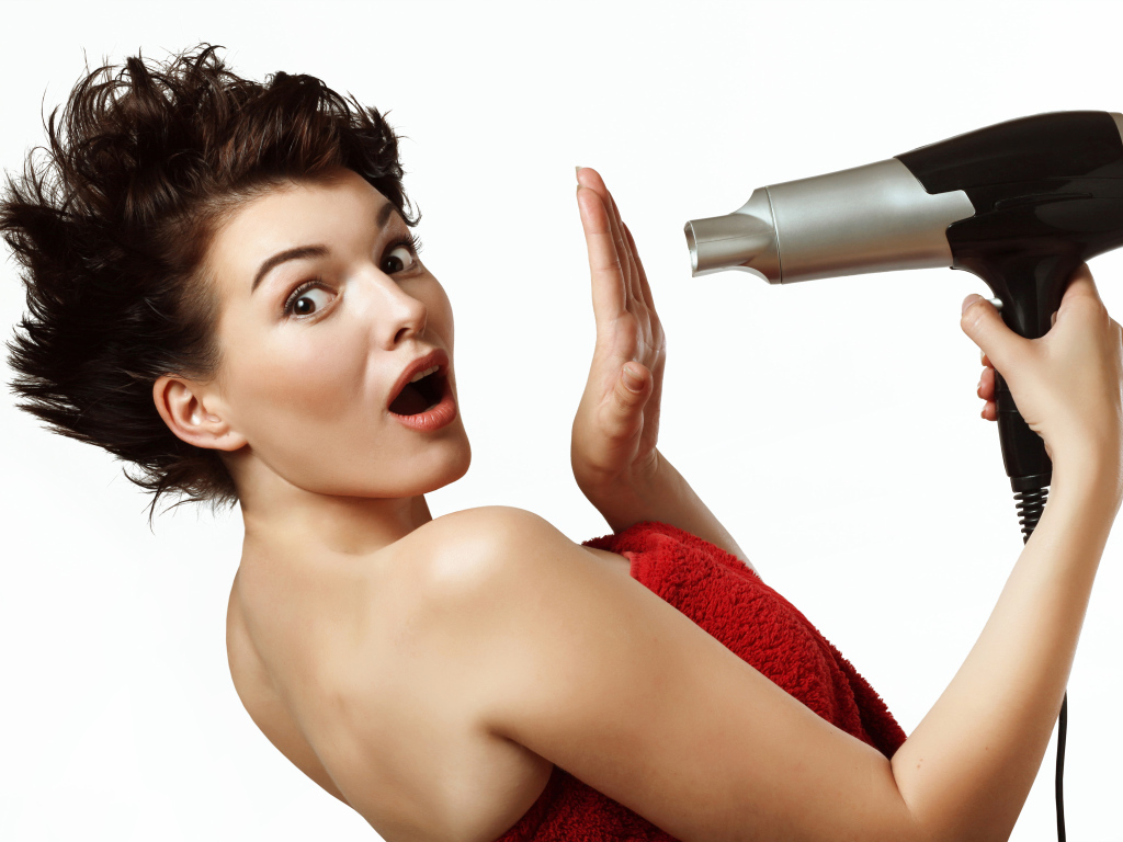 Удивленная девушка с феном в руках на белом фоне