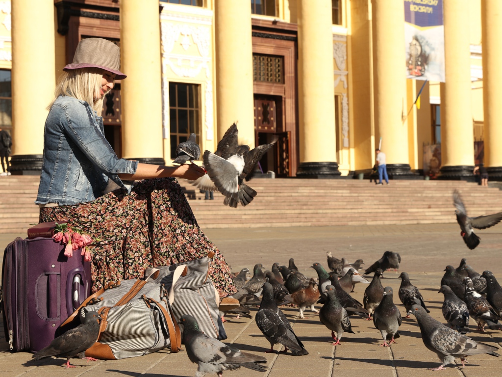 Молодая девушка кормит голубей на вокзале