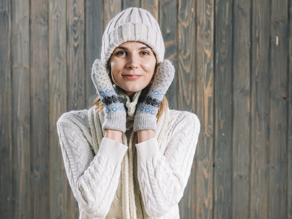 Молодая девушка на шапке, варежках  и теплой шапке на фоне забора