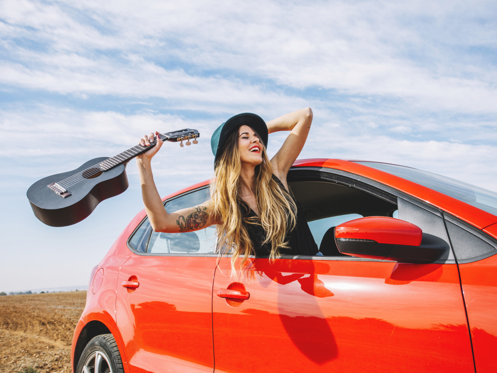 Молодая девушка с гитарой в красной машине летом