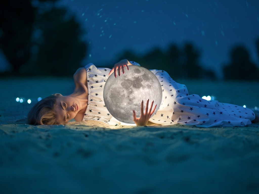 Молодая девушка с луной в руках лежит на песке